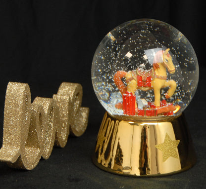Schneekugel Schaukelpferd rot gold mit Geschenken Sockel gold mit Sternen mit Spieluhr 12 cm Durchmesser - Schneekugelhaus